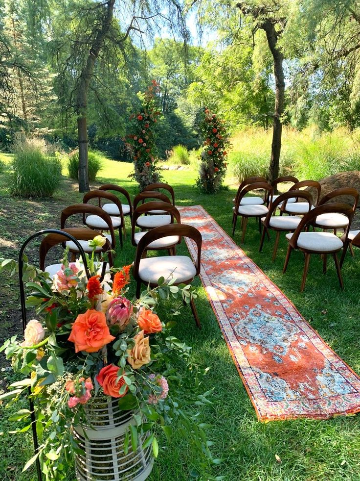 an outdoor ceremony set up with chairs, rugs and flowers on the grass in front of trees