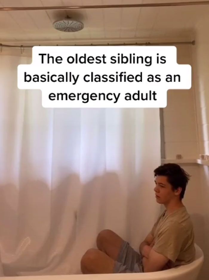 a man sitting on top of a bath tub next to a shower curtain with the words, the oldest sibling is basically classified as an emergency adult