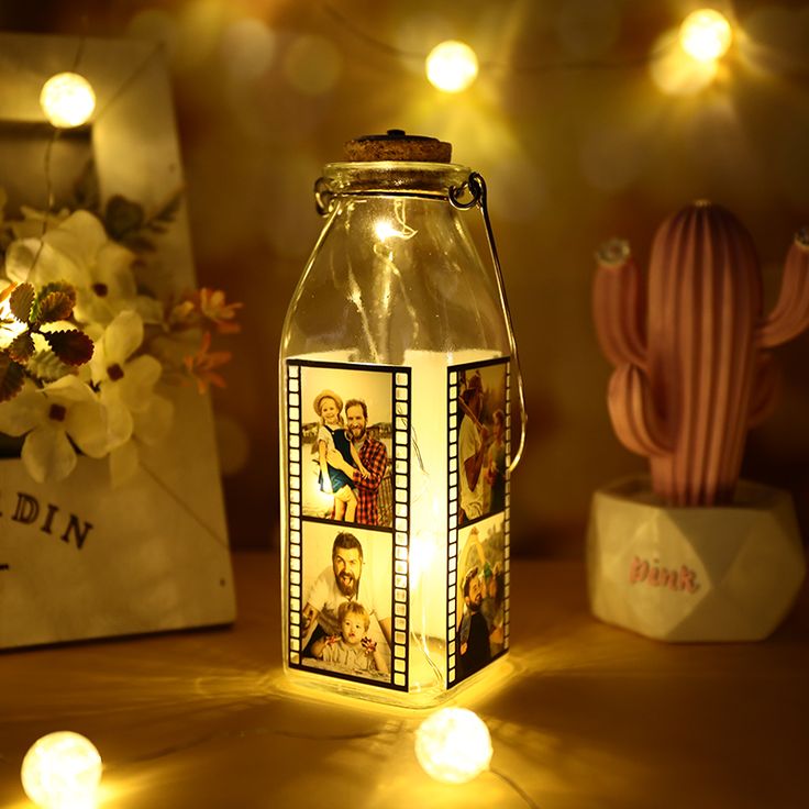 a glass jar with pictures on it sitting next to a cactus