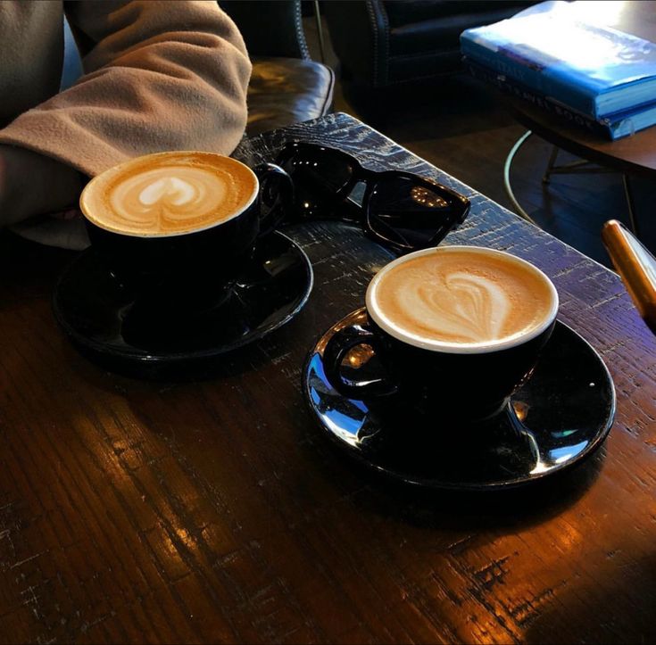 two cups of cappuccino sitting on top of black saucers