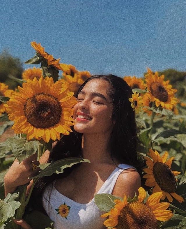 a woman standing in a field of sunflowers with her face close to the camera