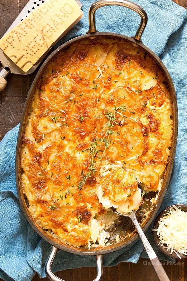 a casserole with cheese and herbs in it on a blue towel next to two spoons