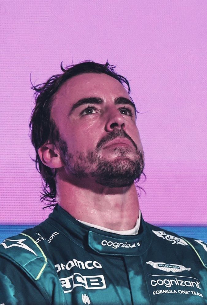 a man with long hair and beard wearing a green racing suit in front of a purple background