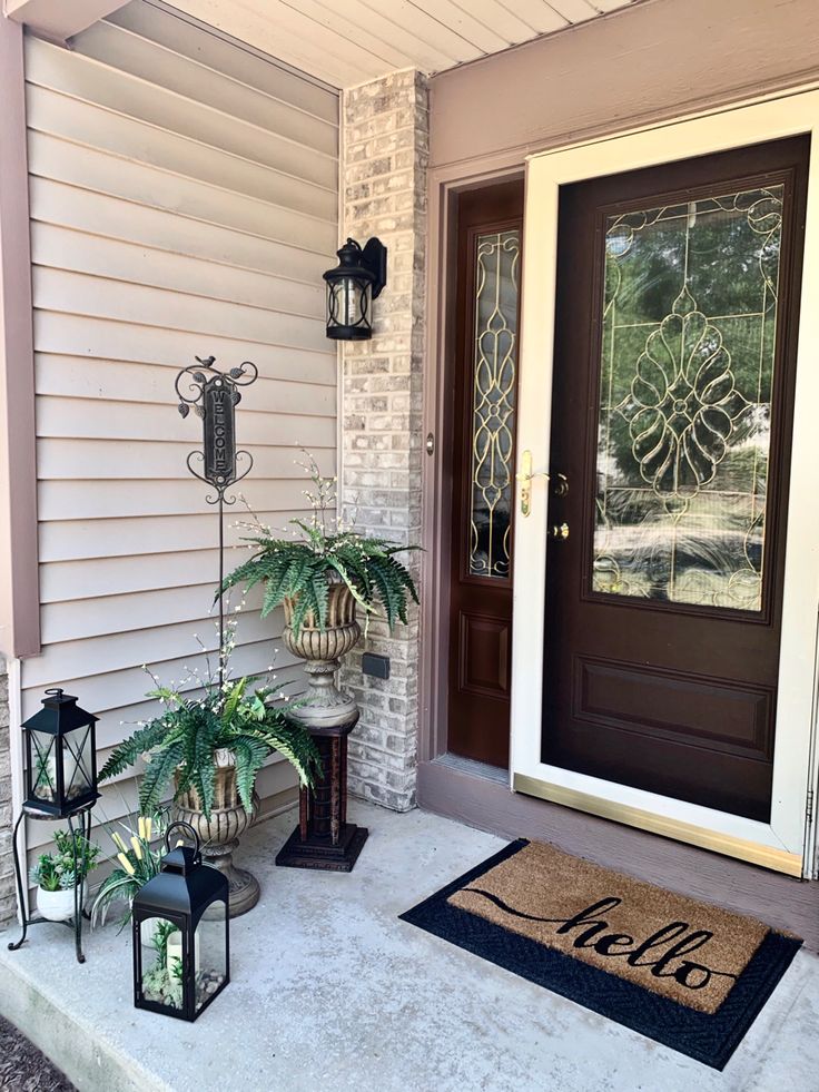 the front porch is decorated with plants, lanterns and an welcome mat that says hello