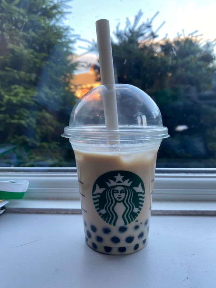 a starbucks drink sitting on top of a window sill next to a cup with a straw in it