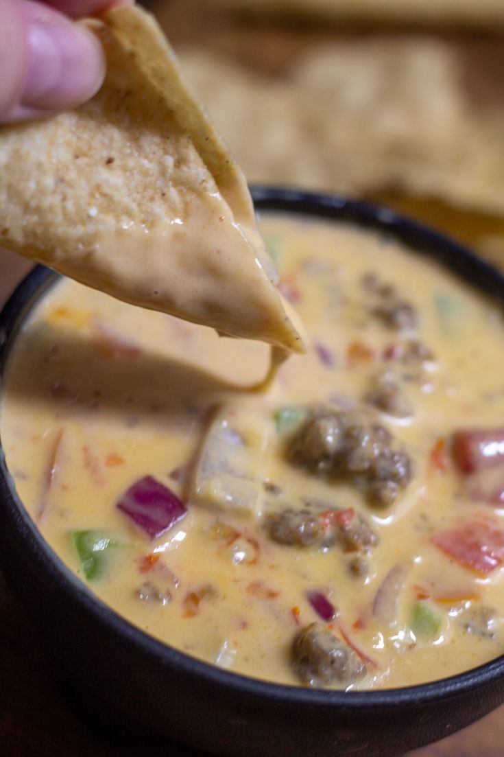 a hand dipping a tortilla chip into a bowl of quesadilla soup