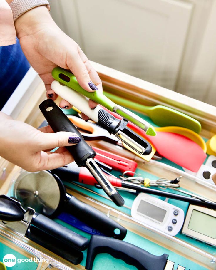 a person is holding scissors in a drawer with other tools on the bottom and inside