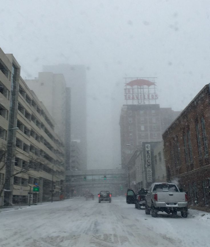 cars driving down a snow covered street with tall buildings in the background