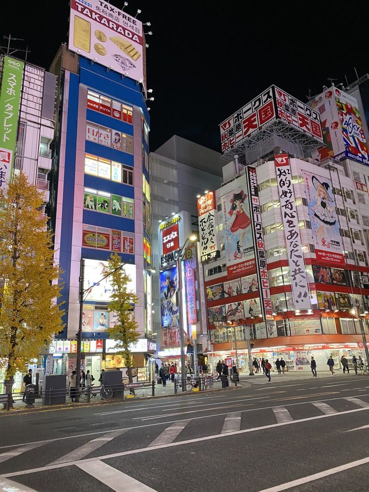 a city street at night with tall buildings and people crossing the street in front of it