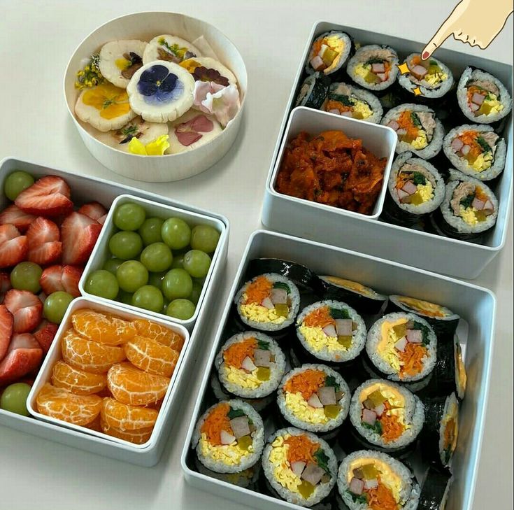 four trays filled with different types of sushi and fruit on top of a table