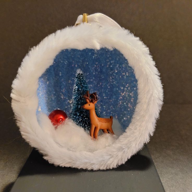 a glass ornament with a deer and christmas tree in the snow on it