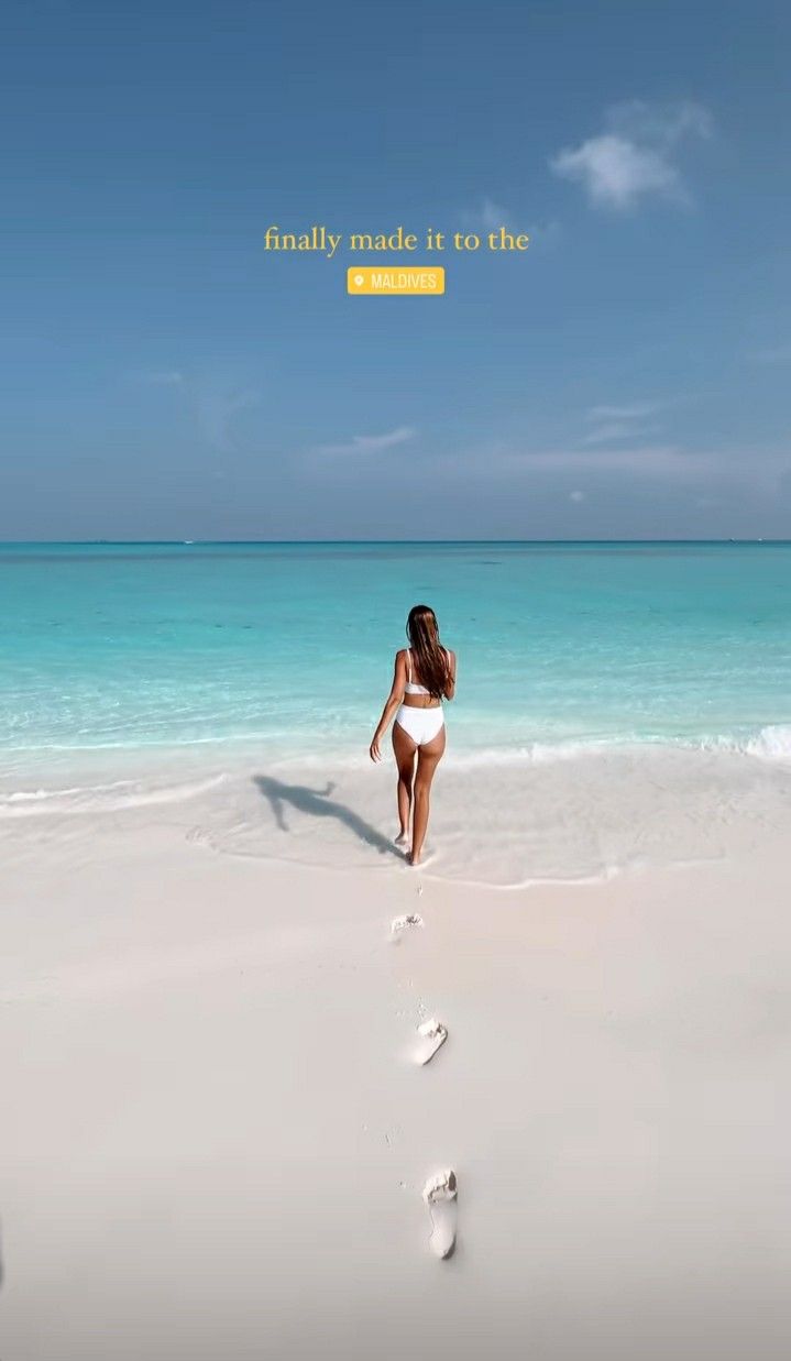 a woman walking on the beach with footprints in the sand and blue water behind her