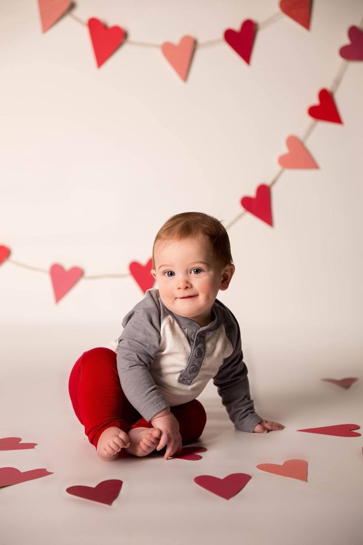 a baby is sitting on the floor with hearts around him and looking at the camera