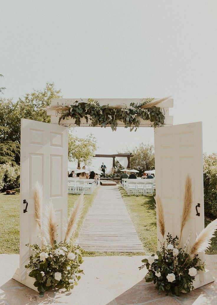 an outdoor wedding ceremony with white flowers and greenery on the aisle, decorated with pamodia