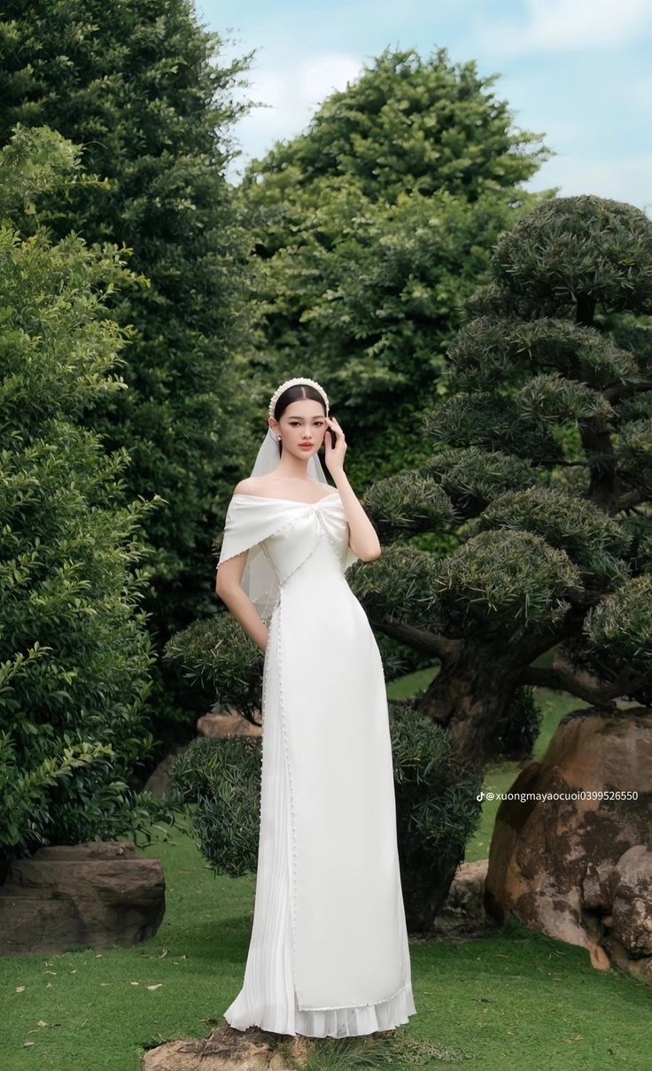 a woman in a white dress is standing on the grass and talking on her cell phone