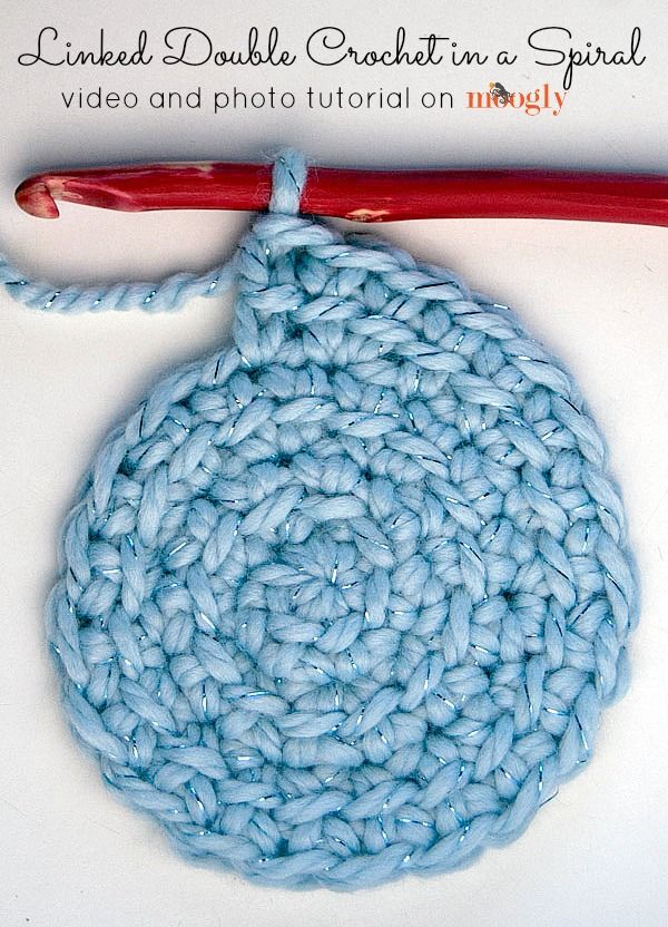 a crocheted blue object is next to a red handled knitting needle on a white surface