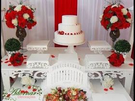 a white table topped with red and white flowers next to a cake on top of it