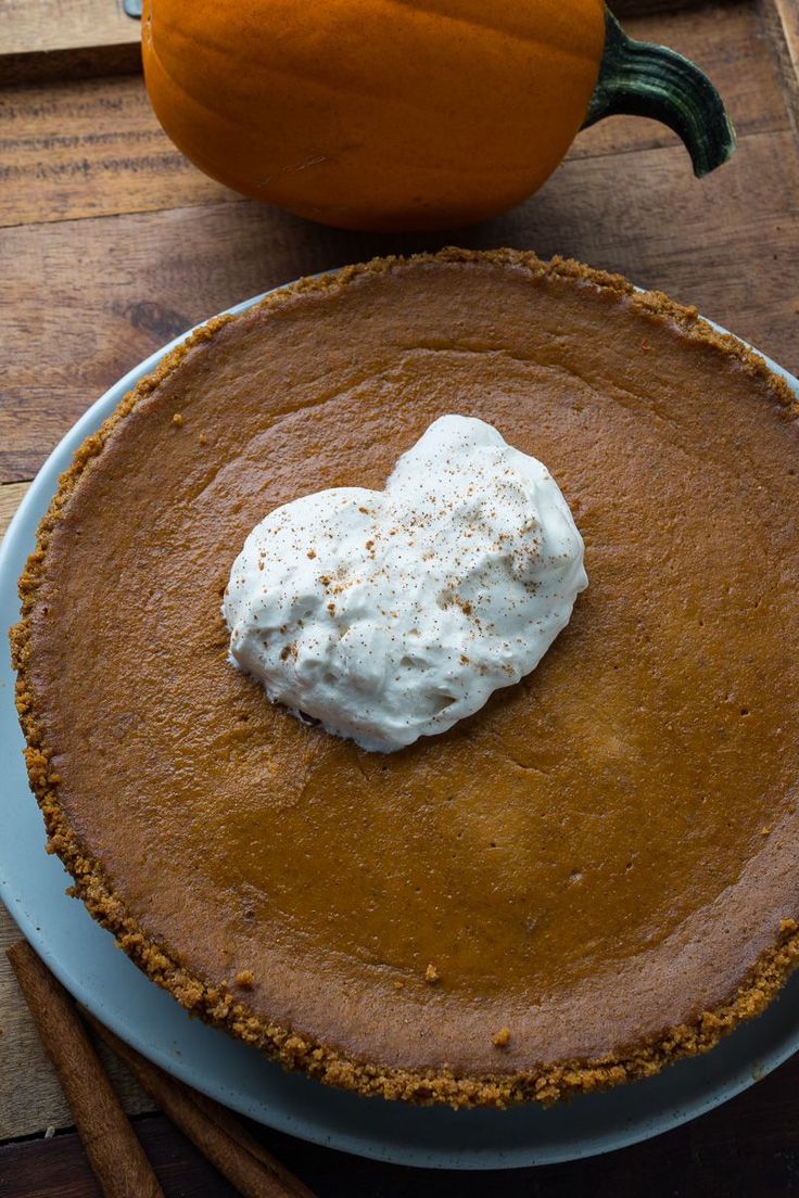 a pumpkin pie with whipped cream in the center on a plate next to an orange pumpkin