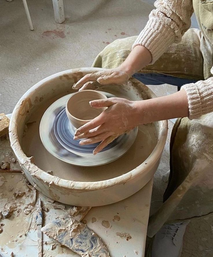 a woman is making a bowl out of clay on a potter's wheel with her hands