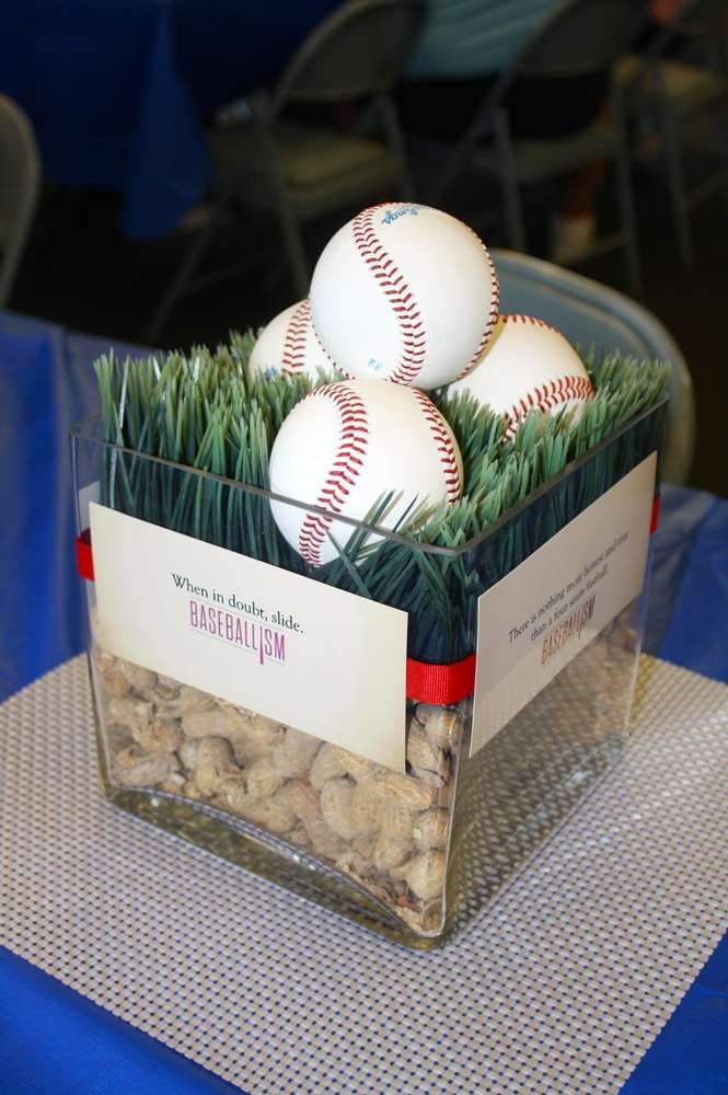 three baseballs are sitting in a clear container on a blue tablecloth with green grass