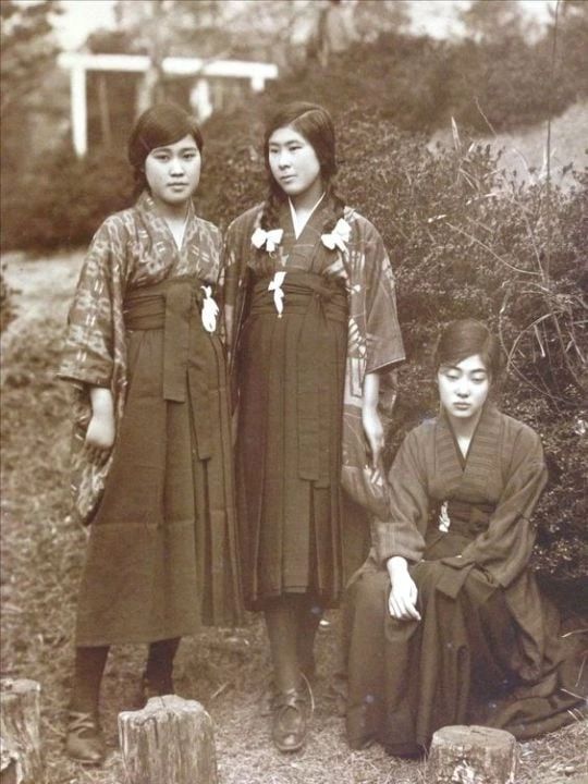 an old photo of three women standing next to each other in front of some bushes