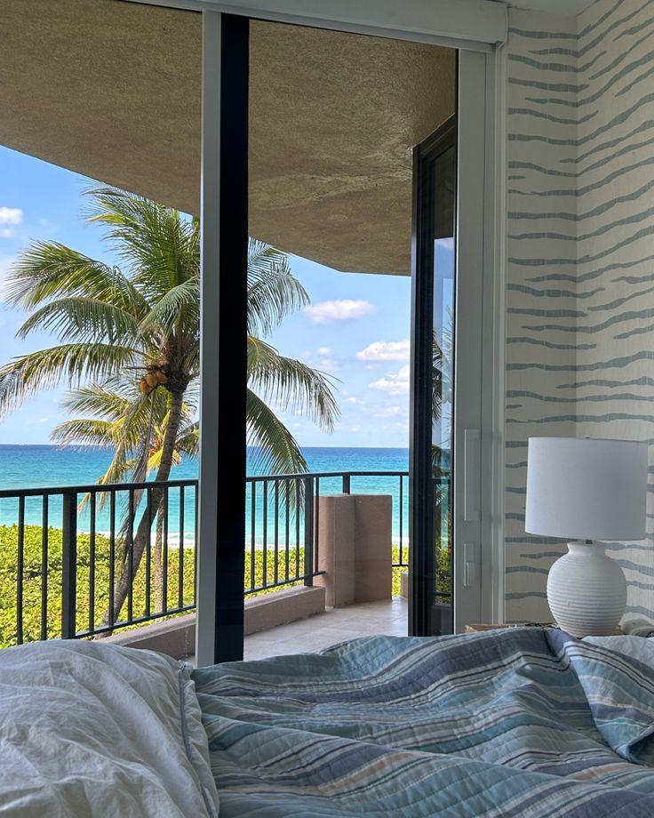 a bedroom with a balcony overlooking the ocean and palm trees in front of an open door