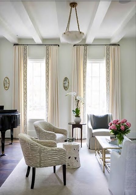 a living room filled with furniture and a piano in front of two windows covered in curtains