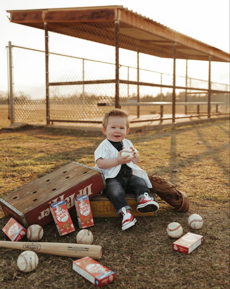 a young boy sitting on top of a wooden box filled with baseballs