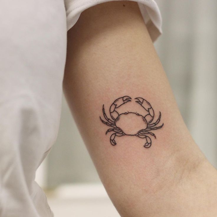 a small crab tattoo on the left inner arm and wrist, done in black ink