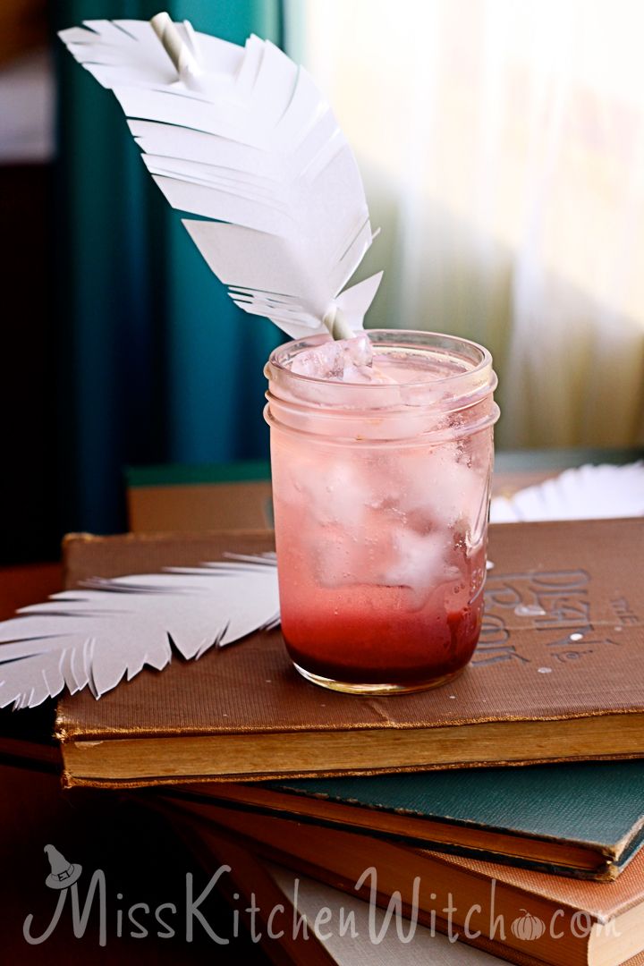 a book with a feather quill sitting on top of it next to a drink