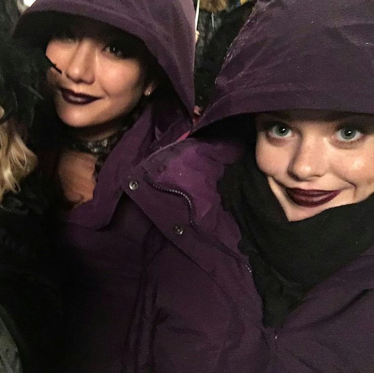 two women wearing purple coats and black scarves are posing for the camera with one woman's face covered in dark lipstick