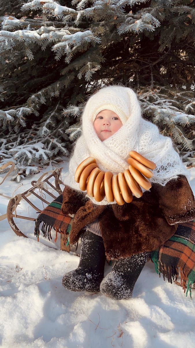 a baby doll sitting in the snow with hot dogs wrapped around it's neck