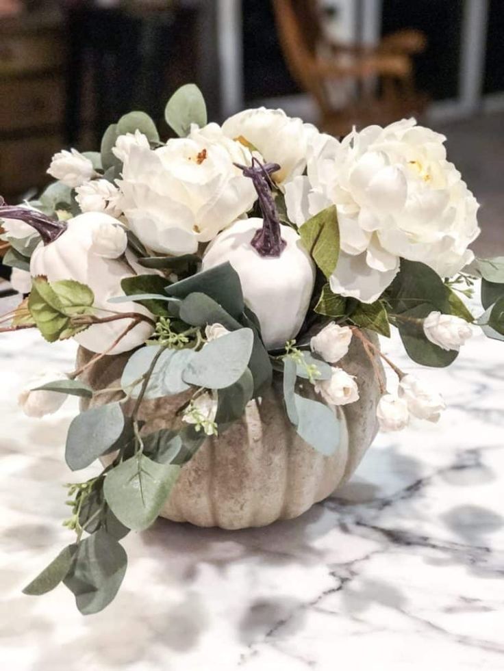 a white pumpkin filled with flowers and greenery on a table in a living room