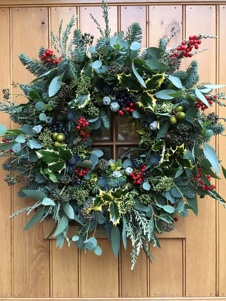 a wreath is hanging on the front door with berries and greenery around it's edges