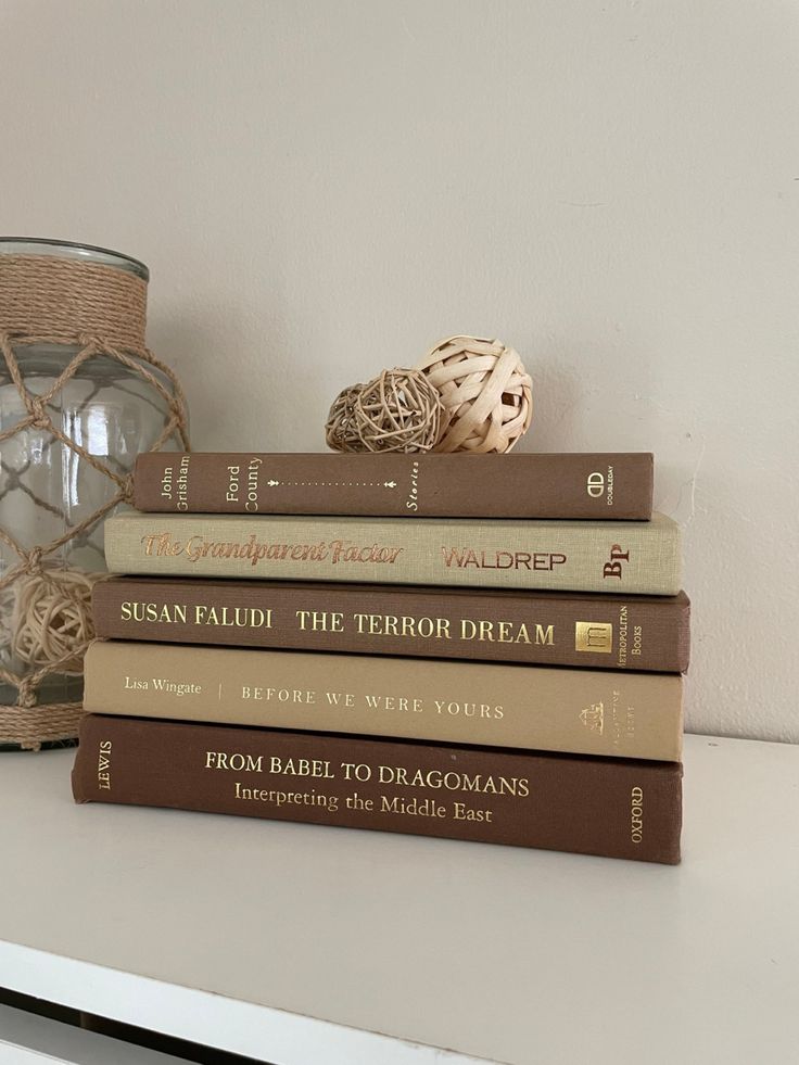 a stack of books sitting on top of a white table next to a glass vase