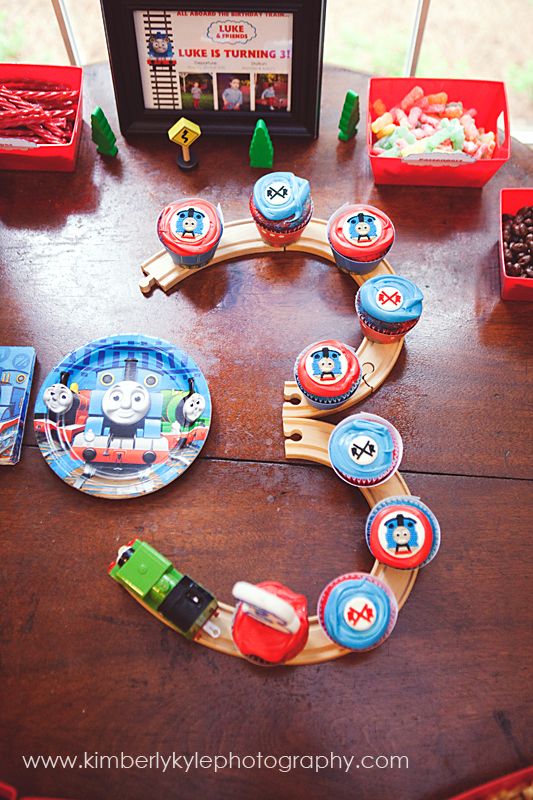 a thomas the train birthday party table with plates and cupcakes on it,