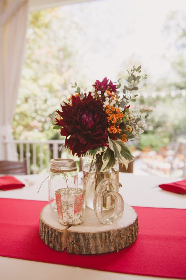 a vase filled with flowers sitting on top of a wooden table covered in red cloth