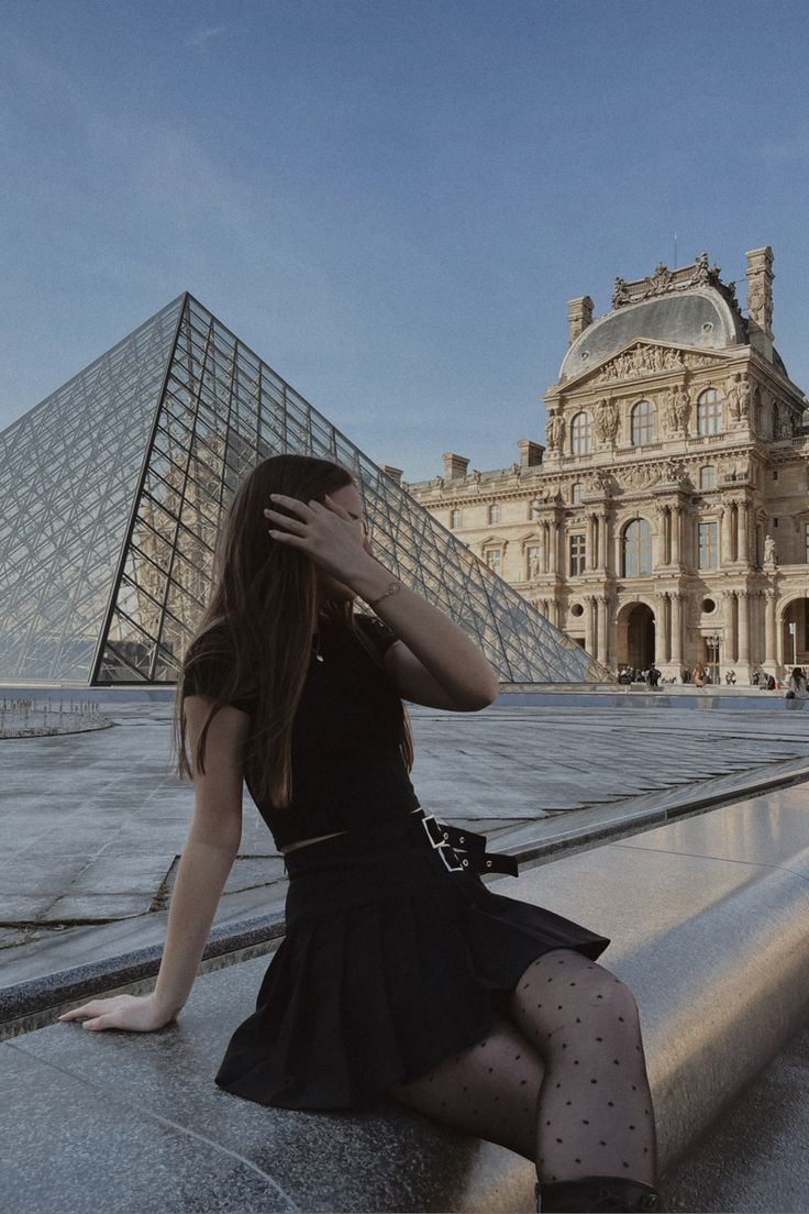 a woman sitting on the ground in front of a building with a pyramid behind her