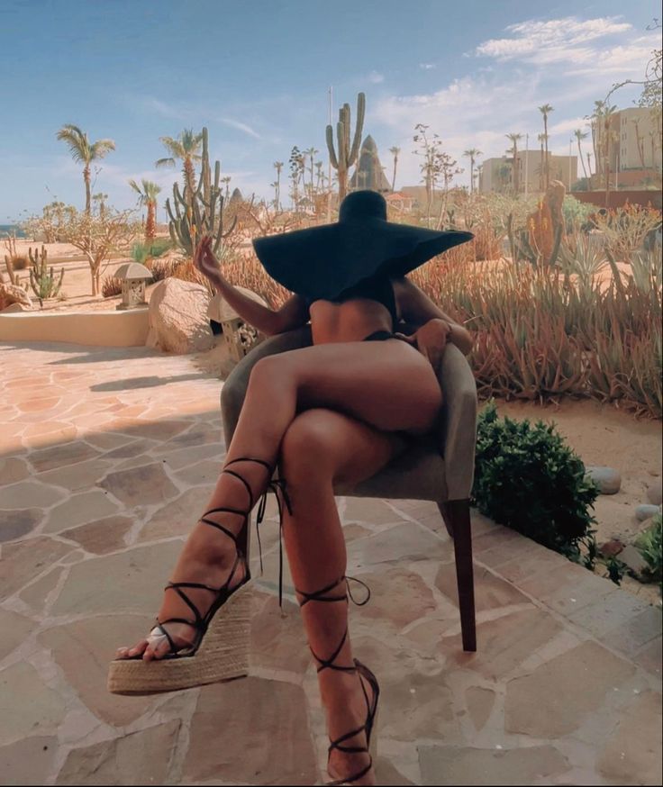 a woman sitting in a chair with her legs crossed wearing sandals and a black hat