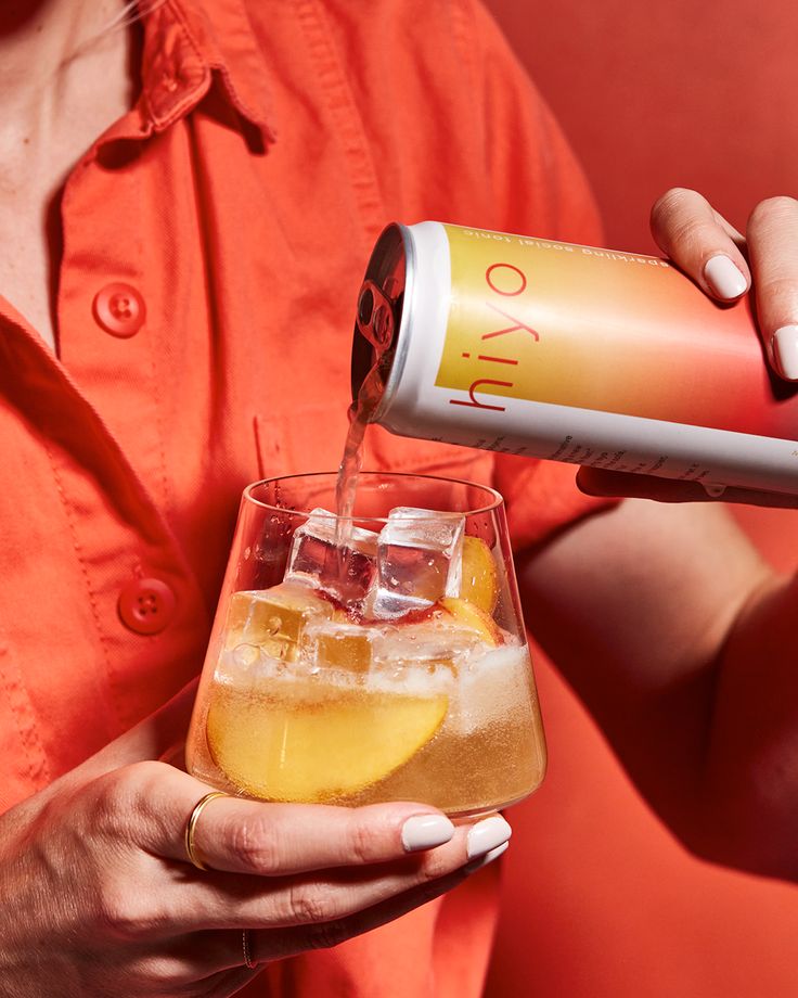 a woman is pouring an alcoholic beverage into a glass with ice and lemon wedges