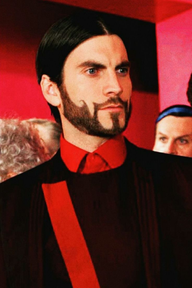 a man with long hair and beard wearing a red tie standing in front of other men