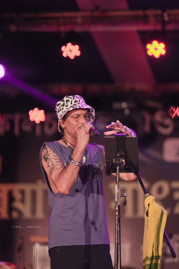 a man standing in front of a microphone with his hand up to his mouth and wearing a bandana on top of his head