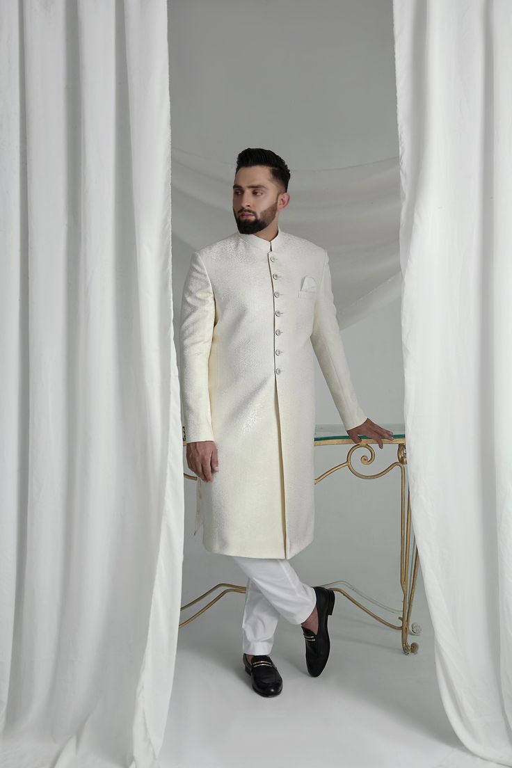 This White Long Sherwani is a stunning choice for your special occasion. Made from printed off-white khaadi silk, it features a silk kurta and cotton pajama for a comfortable fit. Complete your look with the elegant organza Rajastjhani kula (turban) and exude an air of style and sophistication. Cream Cotton Silk Kurta With Traditional Drape, Cream Cotton Silk Traditional Wear For Wedding, Elegant Cotton Silk Kurta With Cutdana, Designer Cotton Bandhgala For Eid, Fitted White Cotton Silk Kurta, White Fitted Cotton Silk Kurta, White Cotton Silk Bandhgala With Resham Embroidery, Elegant Cream Cotton Silk Traditional Wear, Festive White Cotton Silk Sherwani