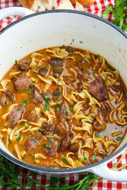 a pot filled with pasta and meat soup on top of a checkered table cloth