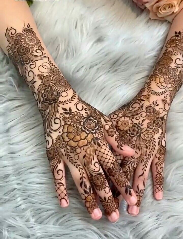 two hands with henna tattoos on them and flowers in the background, one is holding out