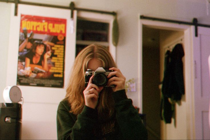 a woman taking a selfie in front of a mirror with a movie poster on the wall behind her