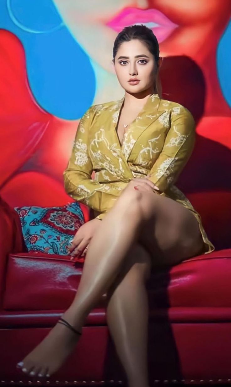 a woman sitting on top of a red couch in front of a colorful wall behind her