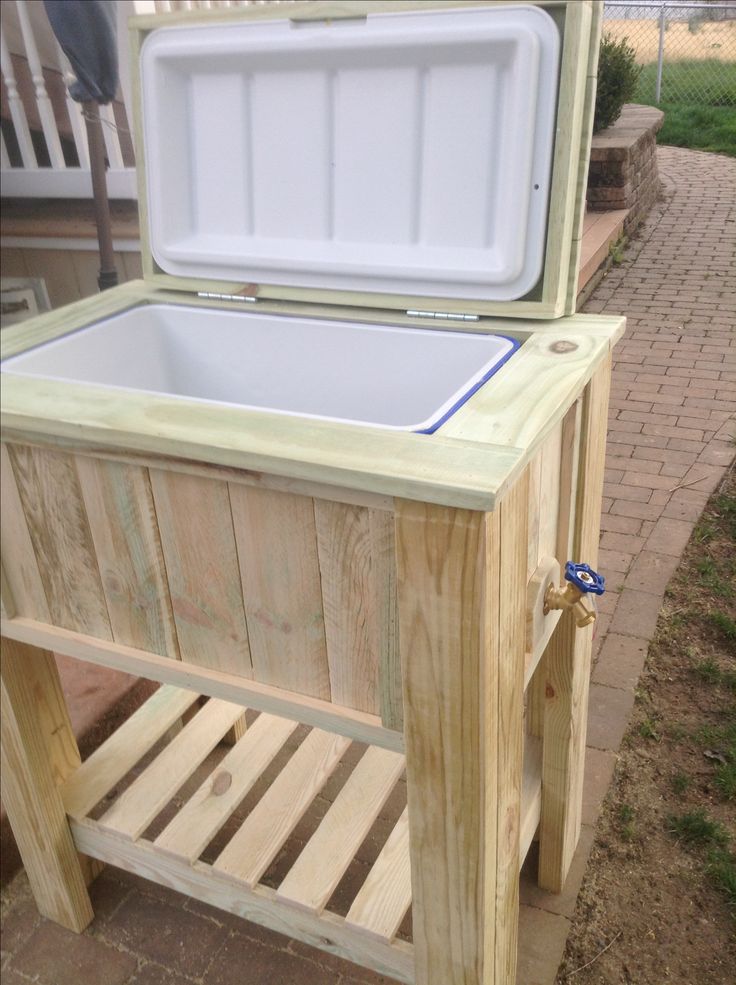 an ice chest sitting on top of a wooden table next to a brick walkway and fence