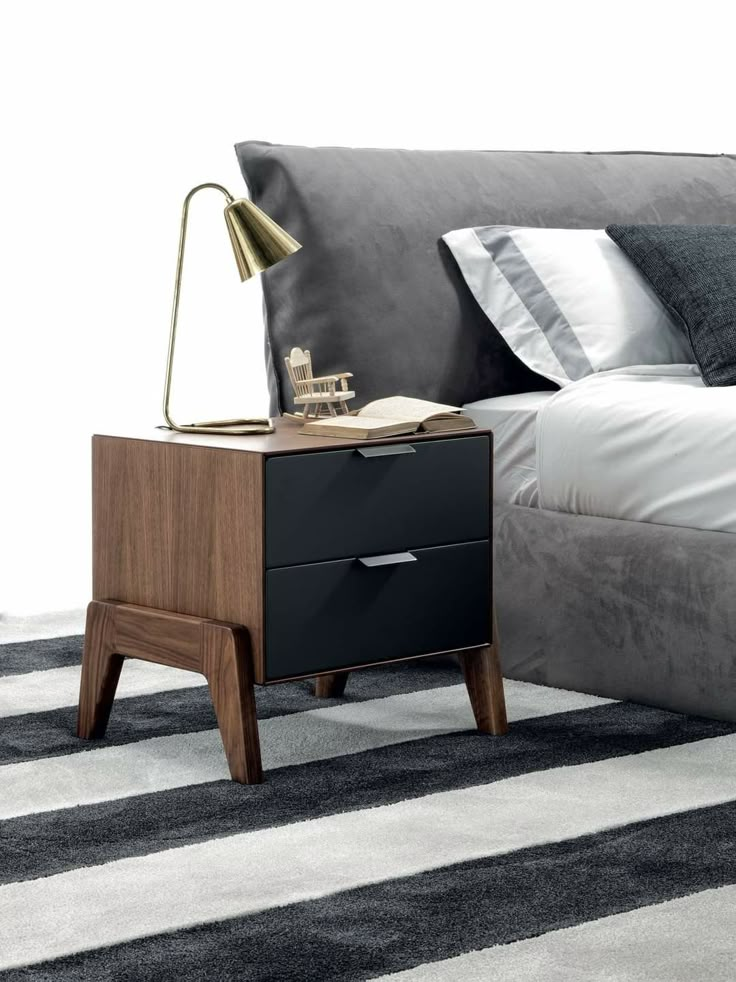 a night stand with two drawers and a lamp next to it on top of a bed