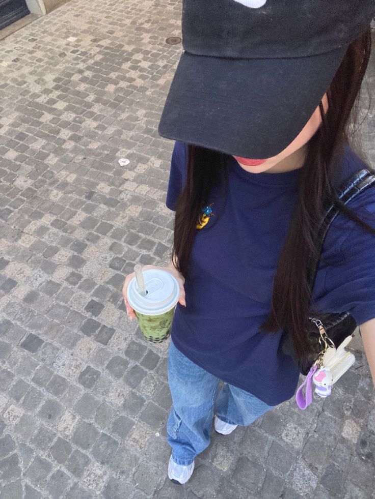 a girl with a hat on and holding a coffee cup in her hand while walking down the street